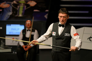 Jimmy White at the 2023 World Seniors Snooker Championship with Philip Williams sat down in the background.